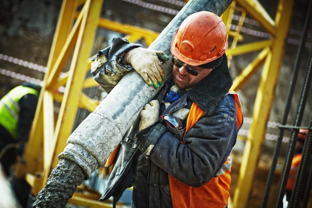 Uomo in un cantiere che ha sulle spalle un grosso tubo per la posa del cemento.