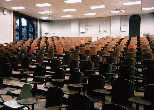 Aula universitaria vuota con molte sedie di legno.